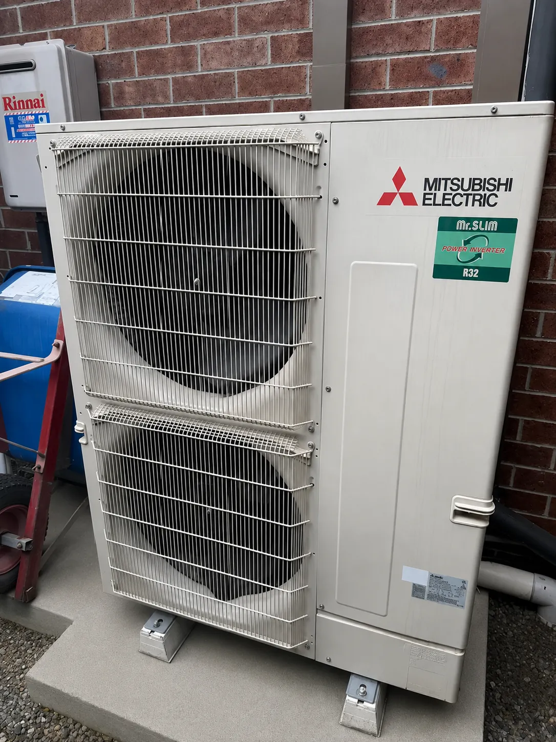Large Mitsubishi Electric ducted outdoor unit installed on a pad against a brick wall