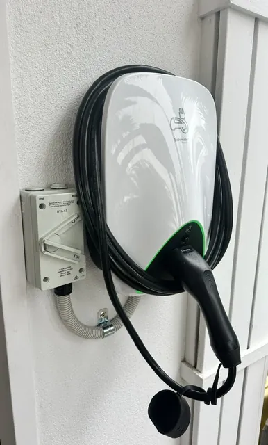 White EV charger mounted on a rendered wall with the charging lead hanging