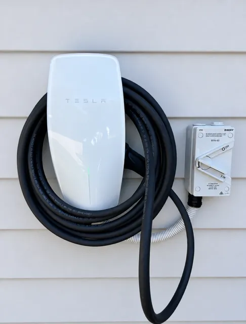 Tesla Wall Connector mounted on white weatherboard cladding with the lead coiled