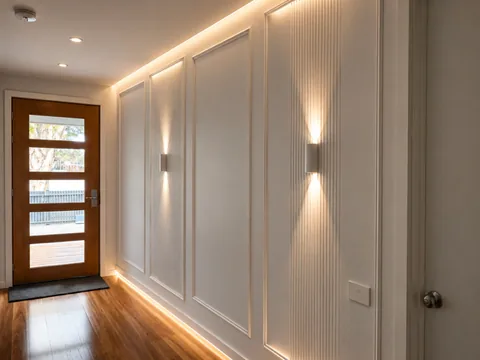 Up and down wall lights lighting a panelled hallway toward a front door